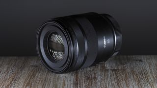 Canon RF 85mm f/2 Macro lens on a table, against a dark backdrop