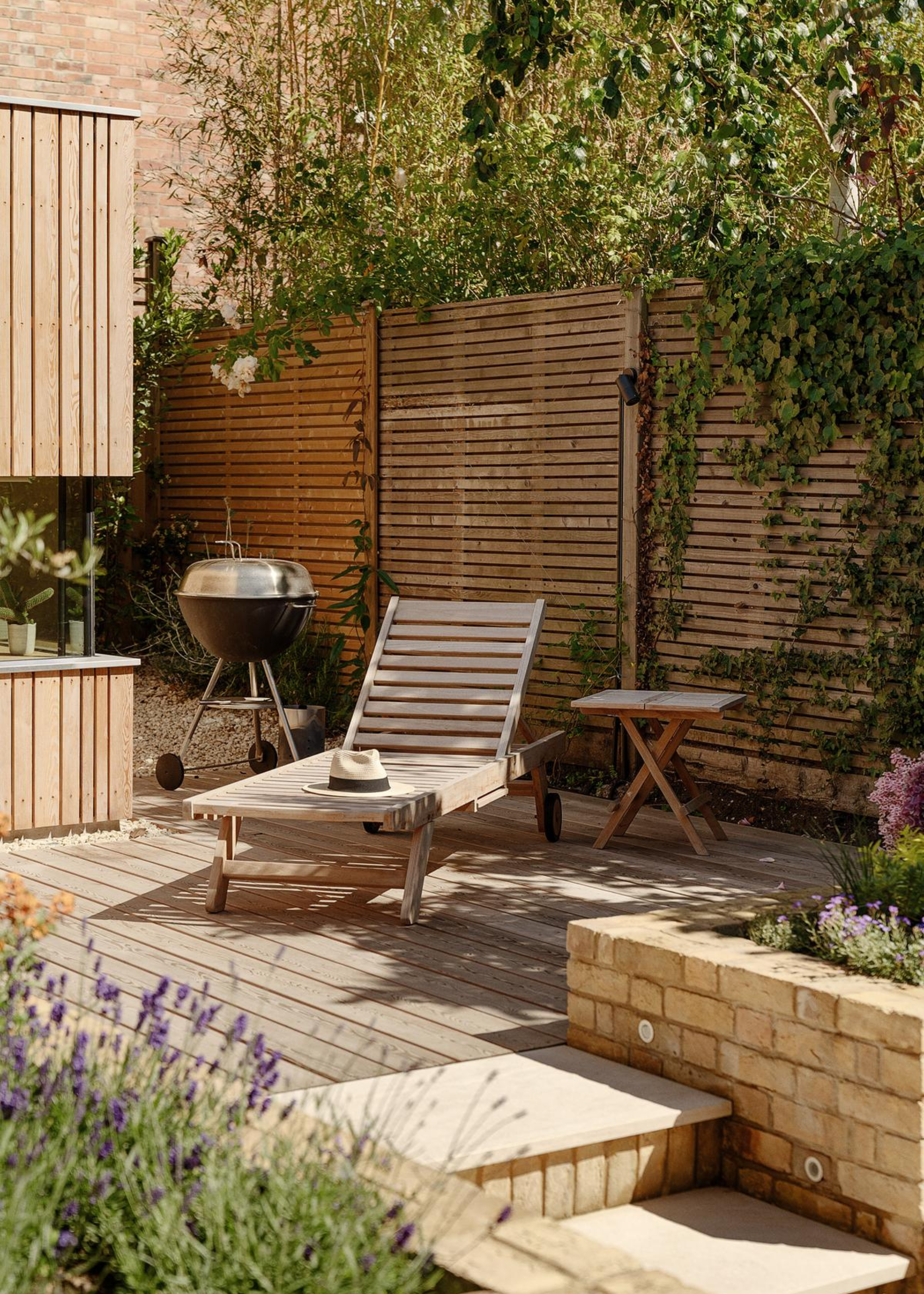 a city urban garden with lavender, a wooden fence, and wooden outdoor furniture, in the corner, you can see the edge of the garden room