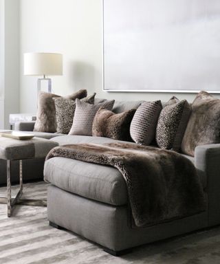 Dark gray sectional with throw pillows in coordinating colors and different textures in room with white wall, and striped area rug