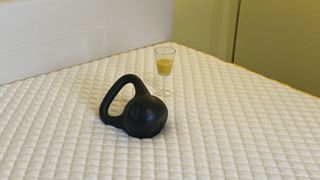 Image shows a black 6kg weight dropped near to a wine glass half full with orange juice during testing of the Eve Premium Hybrid mattress