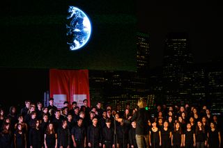 Composer Eric Whitacre leads the LaGuardia High School Senior Chorus for the live performance at the tail end of his audiovisual presentation, "Deep Field: The Impossible Magnitude of our Universe," held on June 1 2019 in Brooklyn Bridge Park.