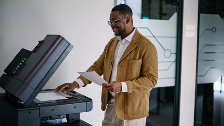 A photo of a businessman making a copy using a modern multifunction printer in an office.