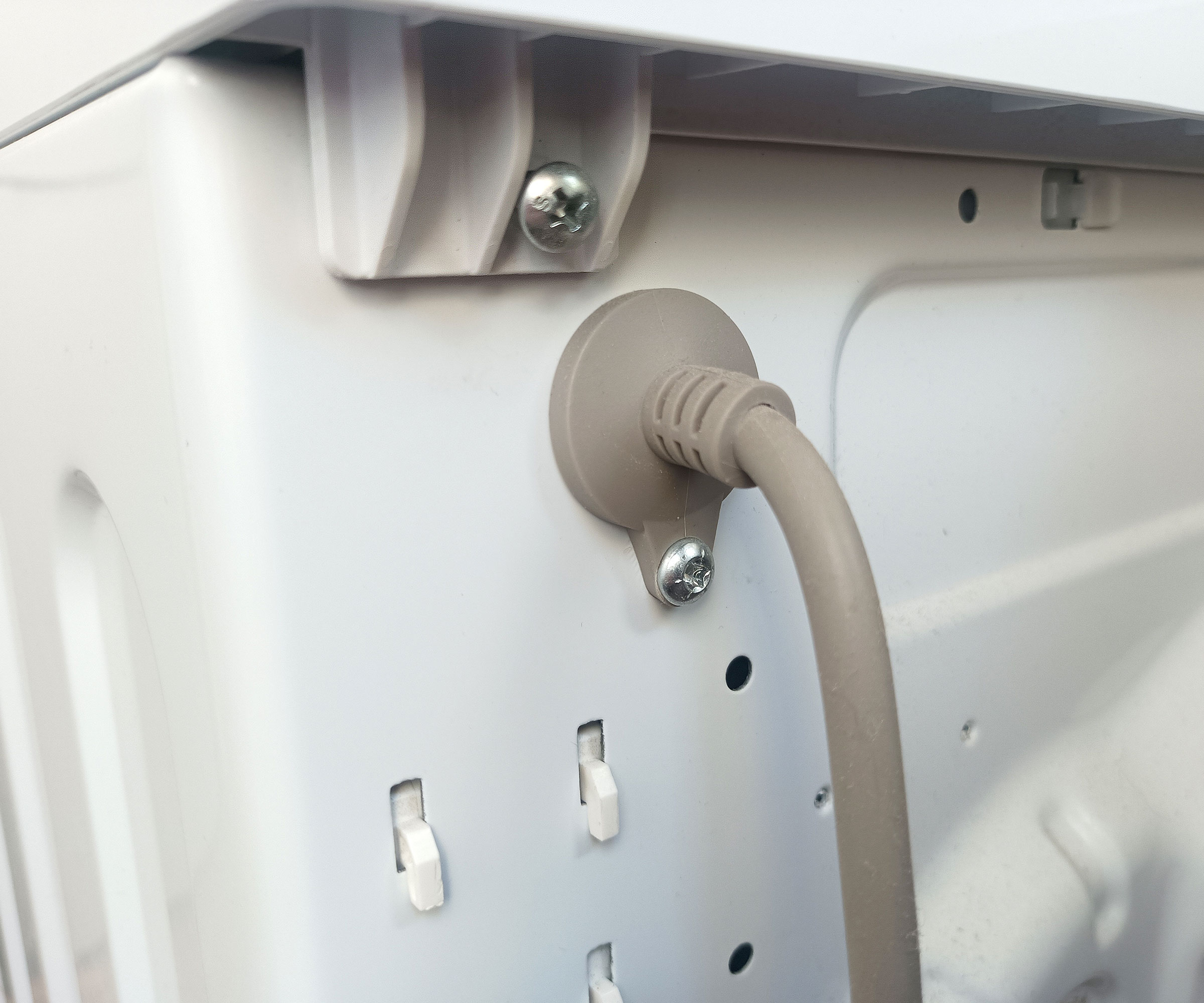 Close up of back of washing machine showing power cable and screw holding lid/top on