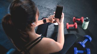 A woman sits and looks at her phone in the gym