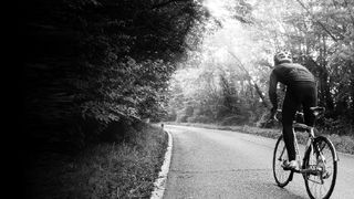 A black and white image of a cyclist riding up a hill on a bike with mudguards