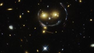 A telescope image of warped yellow starlight forming a smily face against a black background