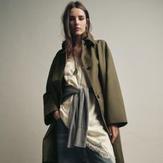 Woman wears green trench coat, silk cami top and blue jeans