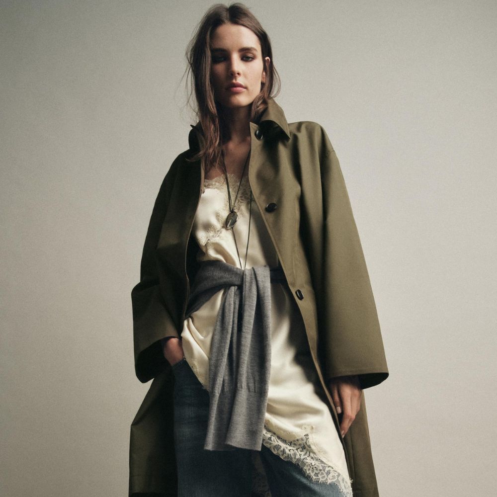 Woman wears green trench coat, silk cami top and blue jeans 