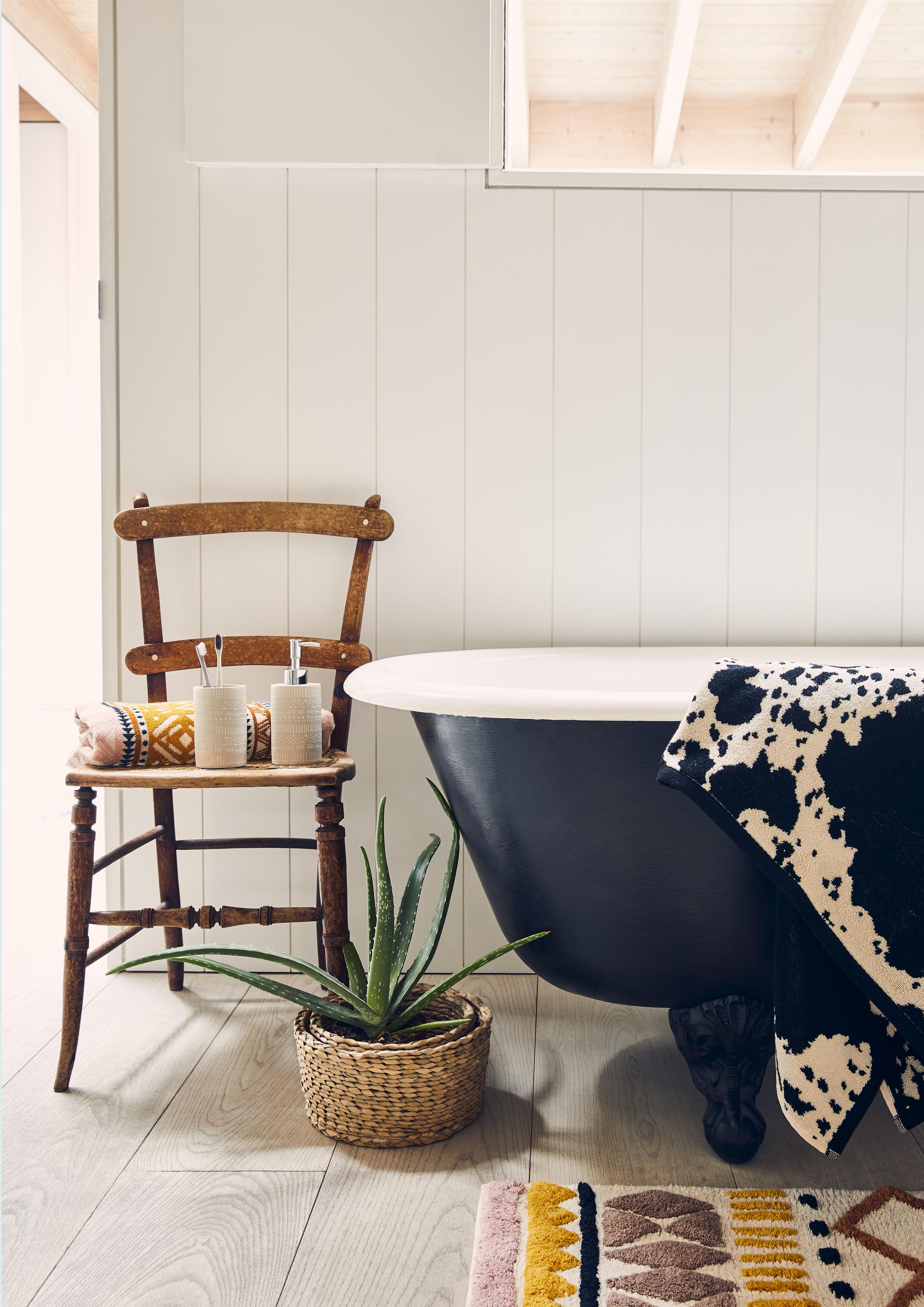 A bathroom idea with black bath and wooden chair with toiletries by George Home