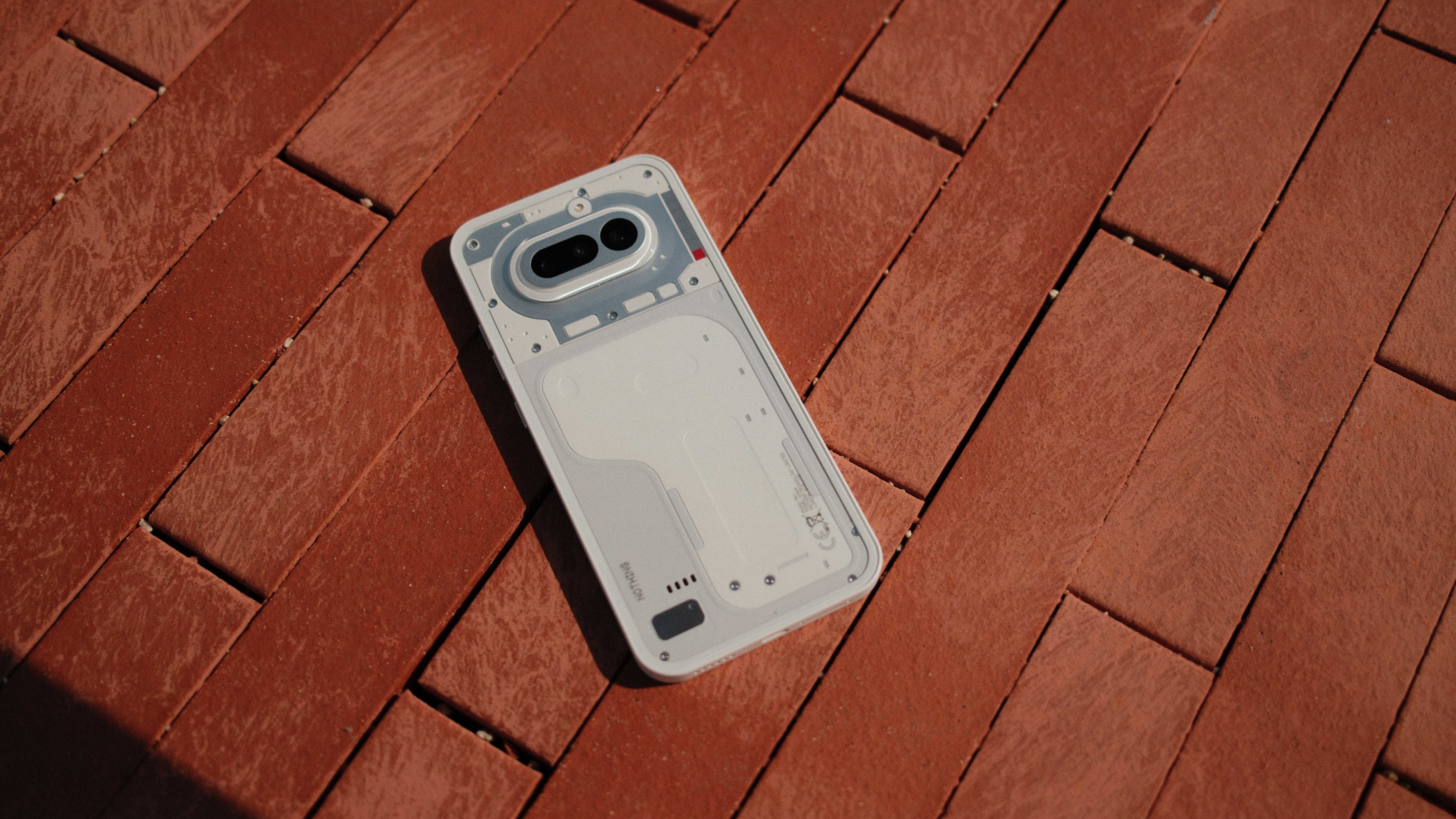 Nothing Phone (4a) placed diagonally on a red brick surface, showing the clean white back panel and exposed design details.