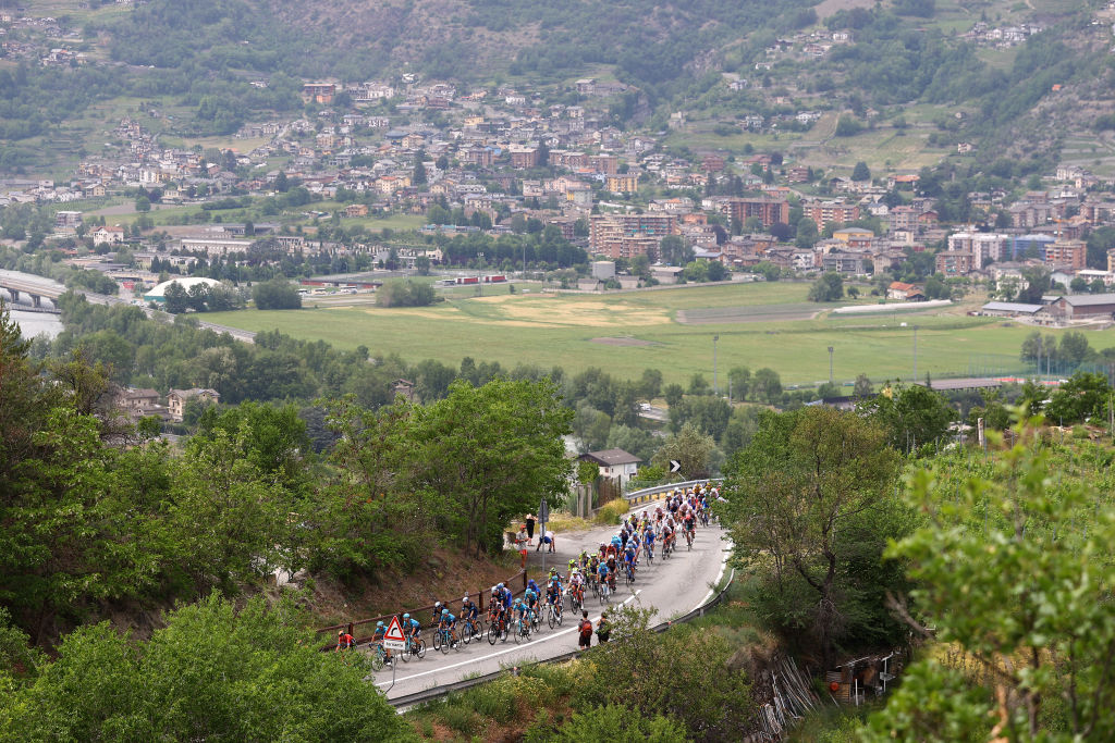 A wide shot showing the peloton winding up a climb to Pila in the 2022 Giro d'Italia, with the countryside in the background