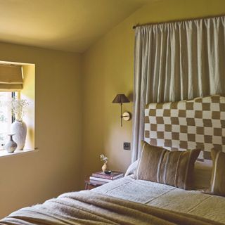 bedroom with yellow painted walls and bed with check headboard with curtain hanging behind the bed