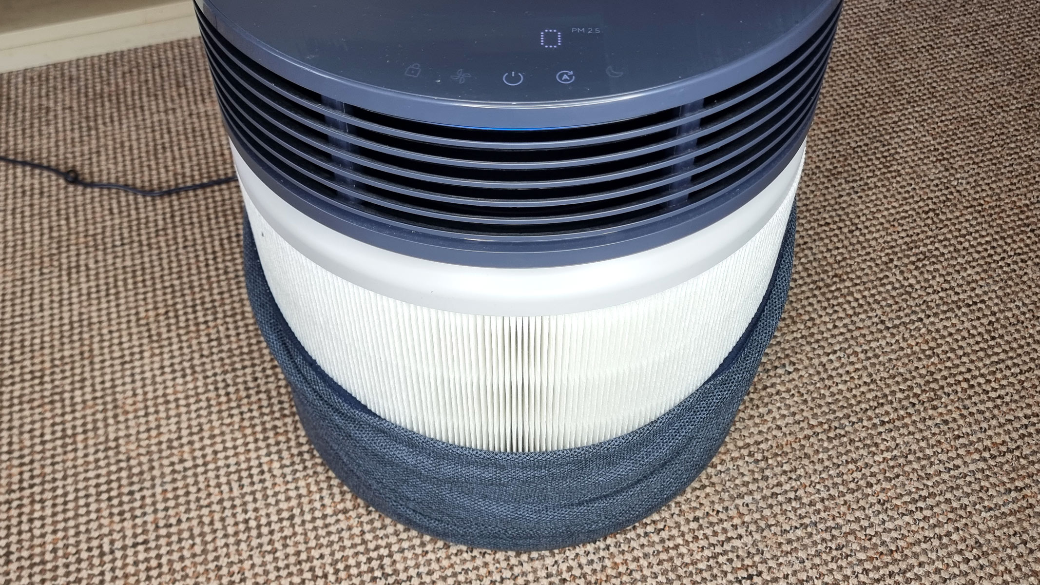 The Blueair Blue Signature air purifier standing in the middle of a living room, with a fabric pre-filter pulled down to expose the HEPA filter underneath