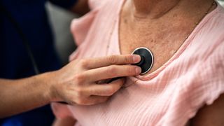 A doctor holds a stethoscope to an older woman's chest