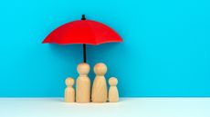 A toy red umbrella is over the heads of a toy wooden family.