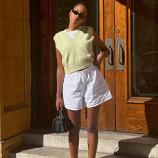 woman wearing yellow vest sweater, white linen shorts, and loafers