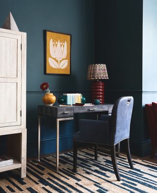 home office with ombre walls, yellow artwork, desk, blue upholstered chair, blue and cream rug, red lamp, storage unit