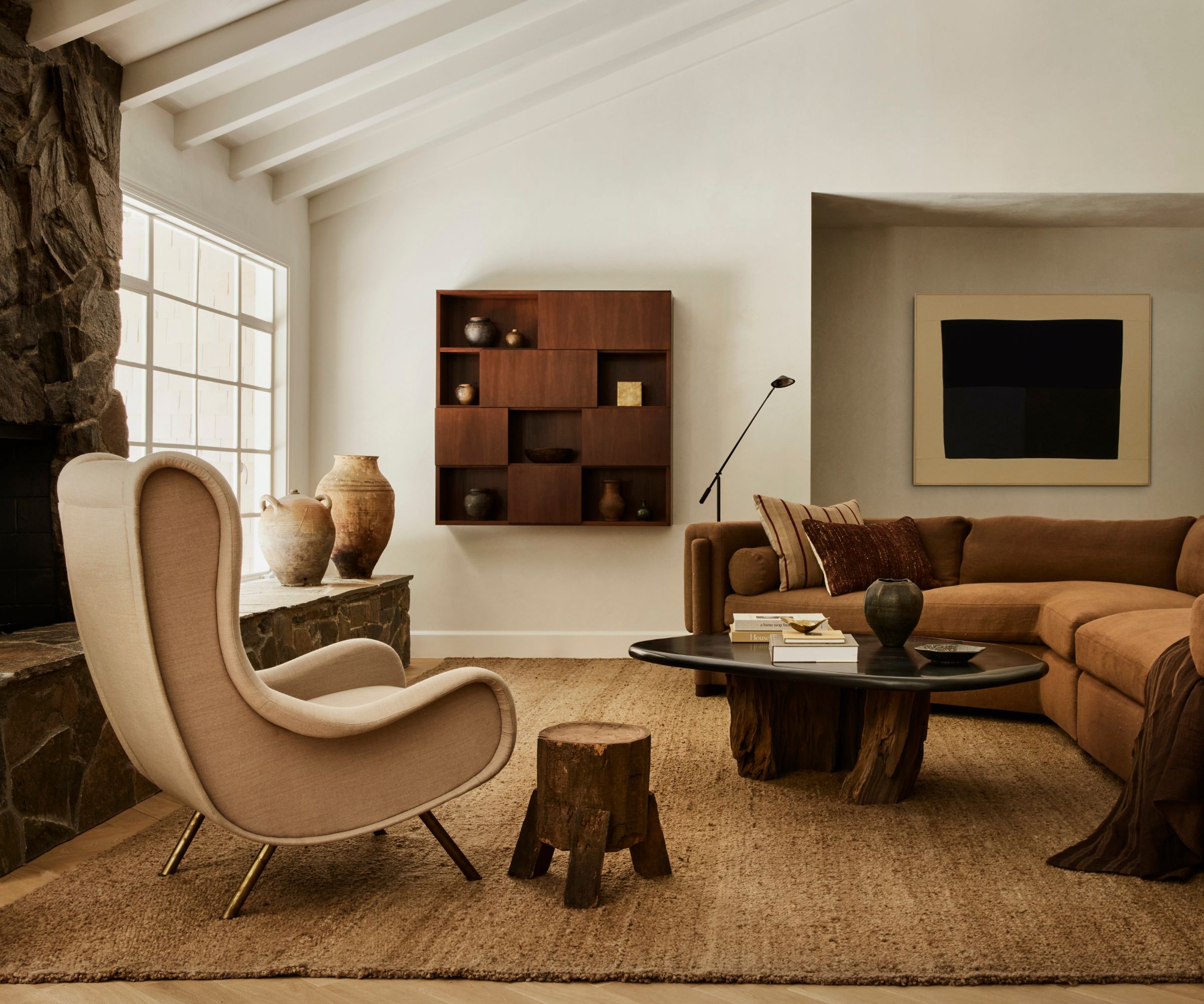 neutral cozy vintage meets modern living room with beamed ceiling, stone full height fireplace, corner sofa, textured woven rug