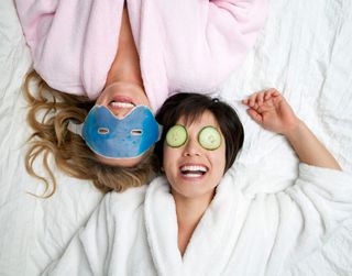 Two women laughing and enjoying face masks with cucumber on their eyes.