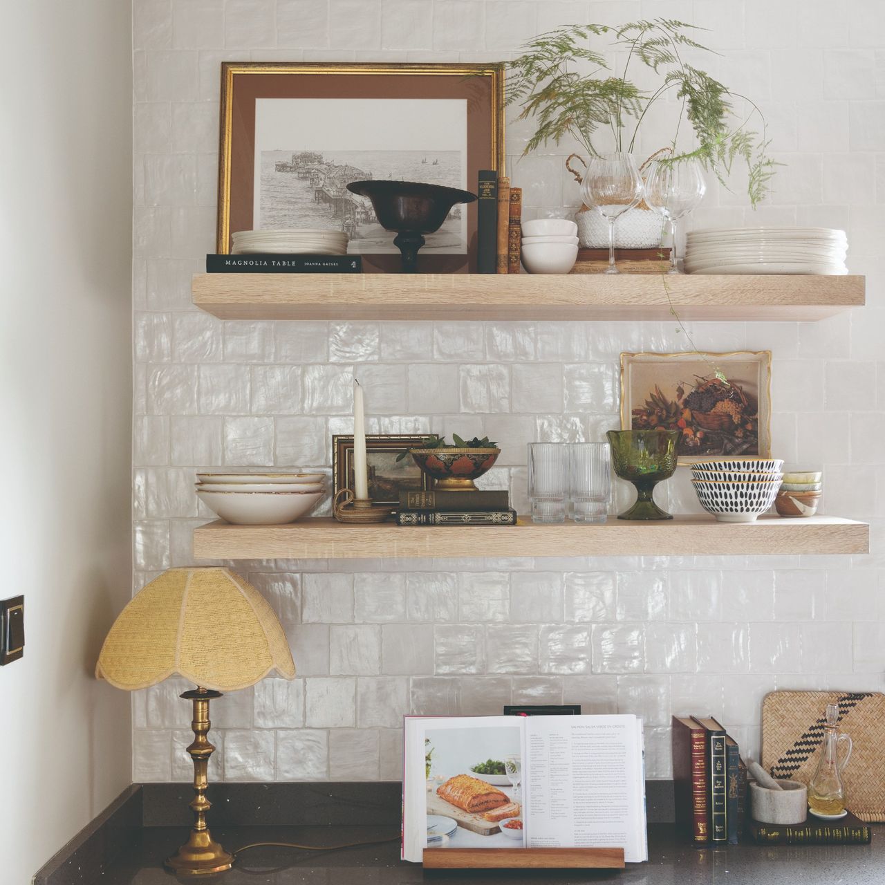 Kitchen shelves displaying tableware with vintage framed art and a fern houseplant