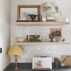 Kitchen shelves displaying tableware with vintage framed art and a fern houseplant