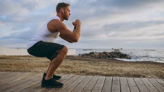 Man performing bodyweight squat outside by the ocean during outdoor workout