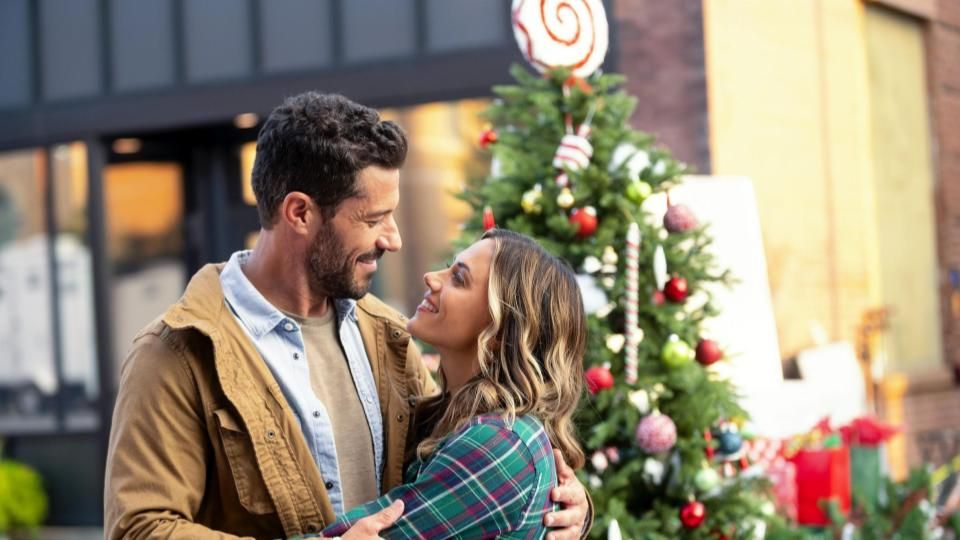 A man and woman look into each other&#039;s eyes lovingly in front of an overdecorated Christmas tree