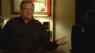 Drew Carey sitting in front of a lamp, with his arm extended in NCIS