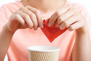 A woman puts artificial sweetener in her coffee.