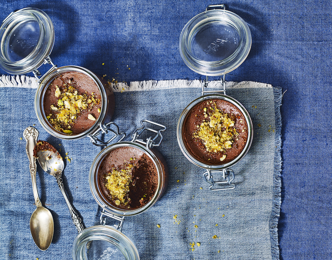 Chocolate Mousse With Honey Hazelnut Praline served in three individual storage jars on a blue tablecloth.