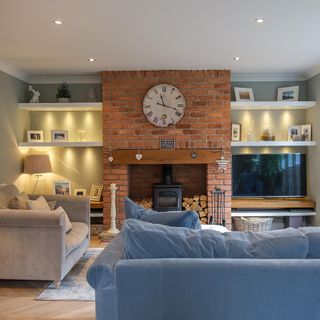 White lounge with brick fireplace, grey sofa, blue sofa and wall shelves