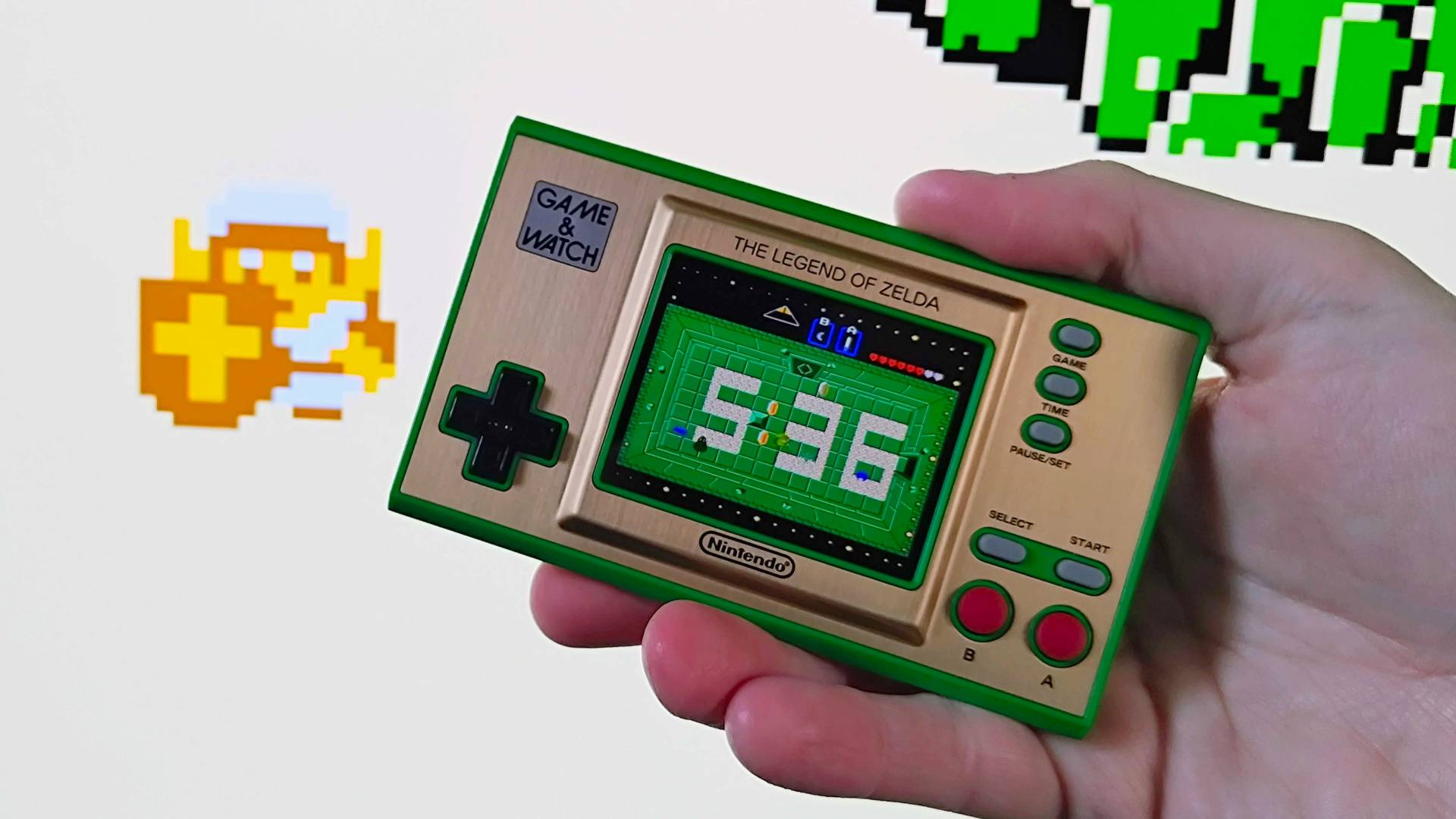 Hand holding Zelda Game and Watch handheld with gameplay featuring Link in white outfit in backdrop.