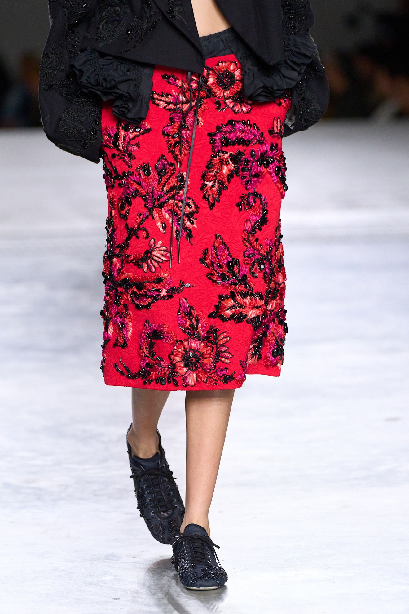 A model at the spring/summer 2026 Dries Van Noten show in Paris wearing a red beaded skirt with black beaded low-profile sneakers.