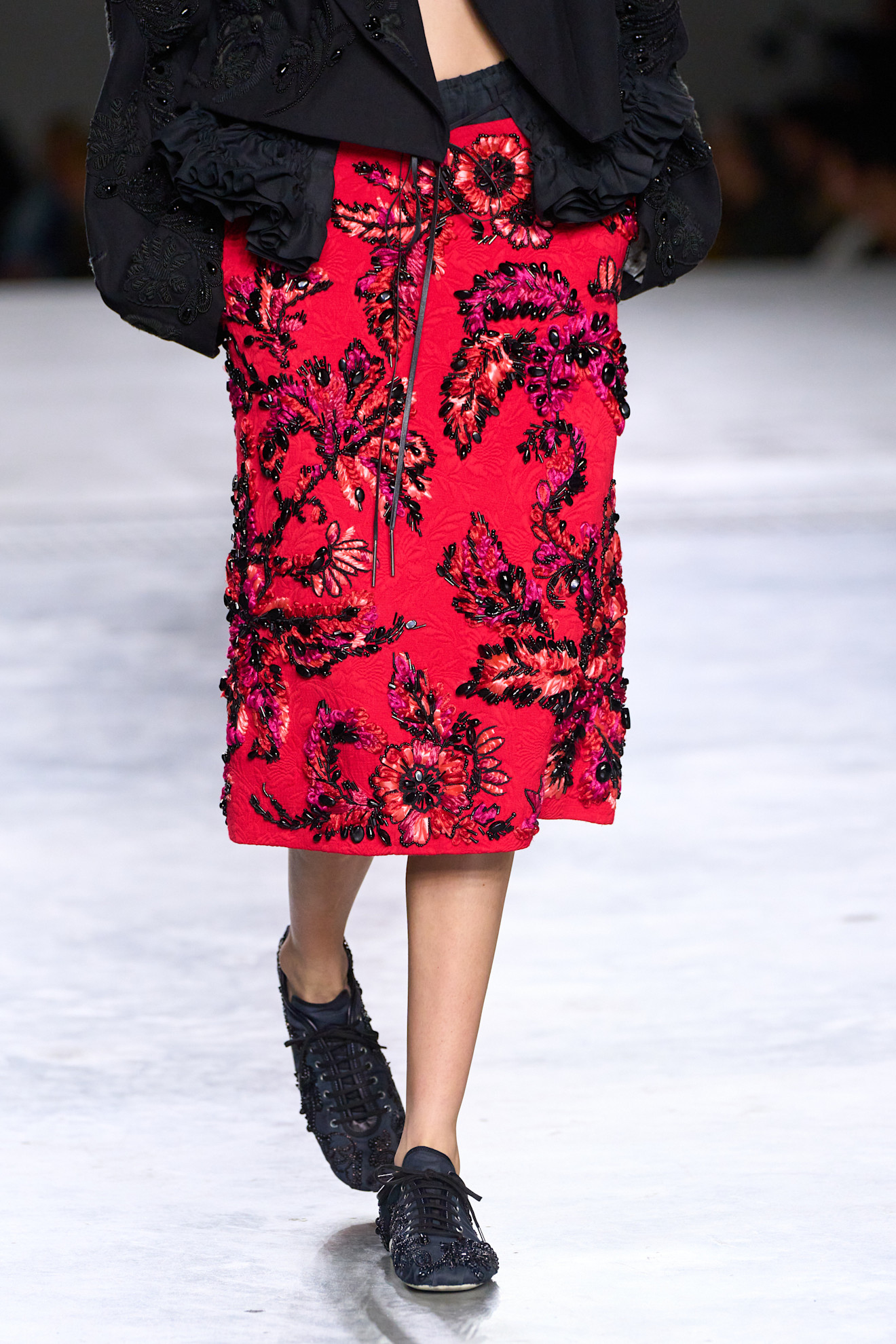 A model at the spring/summer 2026 Dries Van Noten show in Paris wearing a red beaded skirt with black beaded low-profile sneakers.
