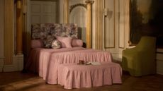 Opulent bedroom area featuring gold-molded walls alongside a pink skirted bed with matching ottoman