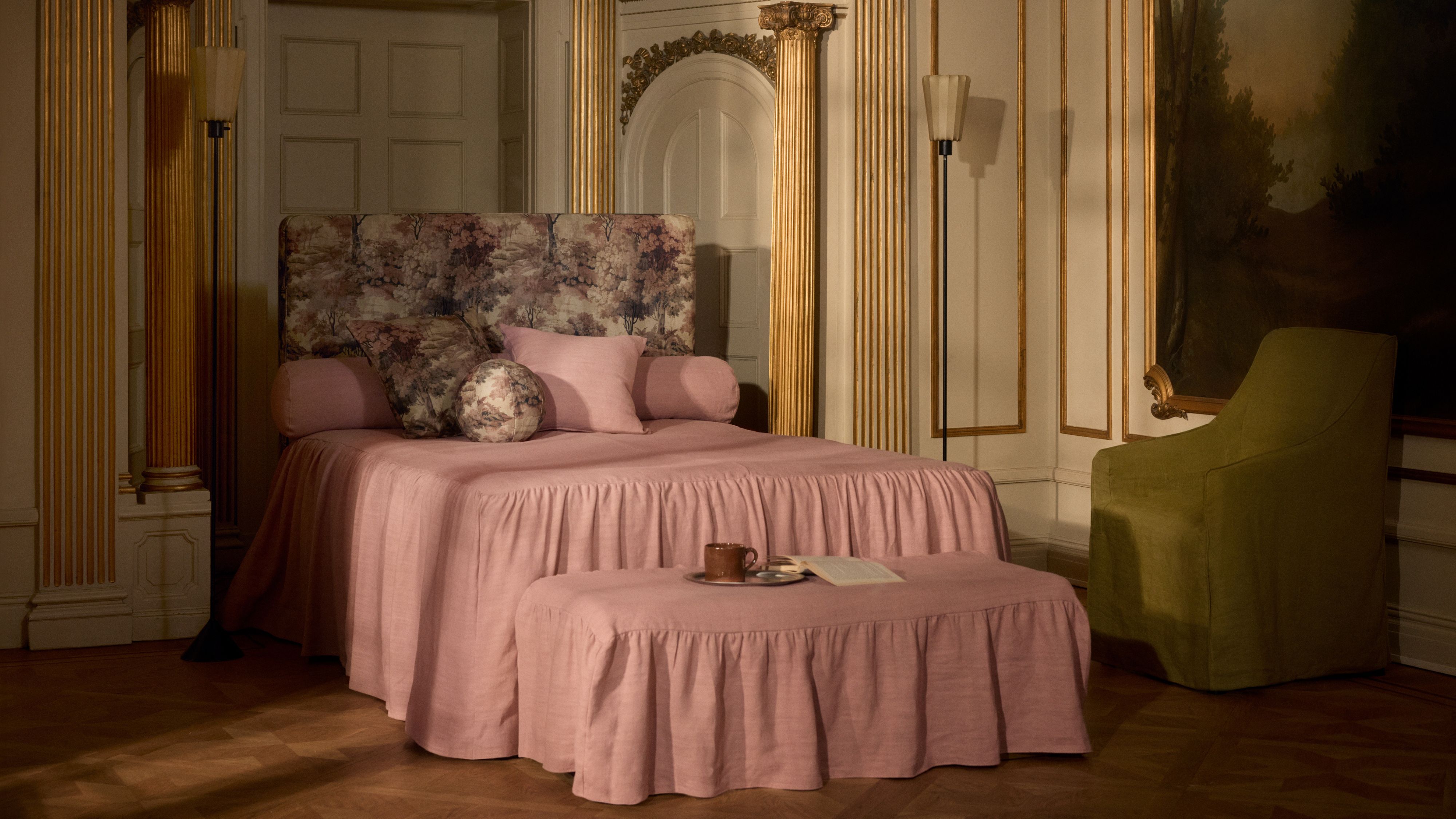 Opulent bedroom area featuring gold-molded walls alongside a pink skirted bed with matching ottoman