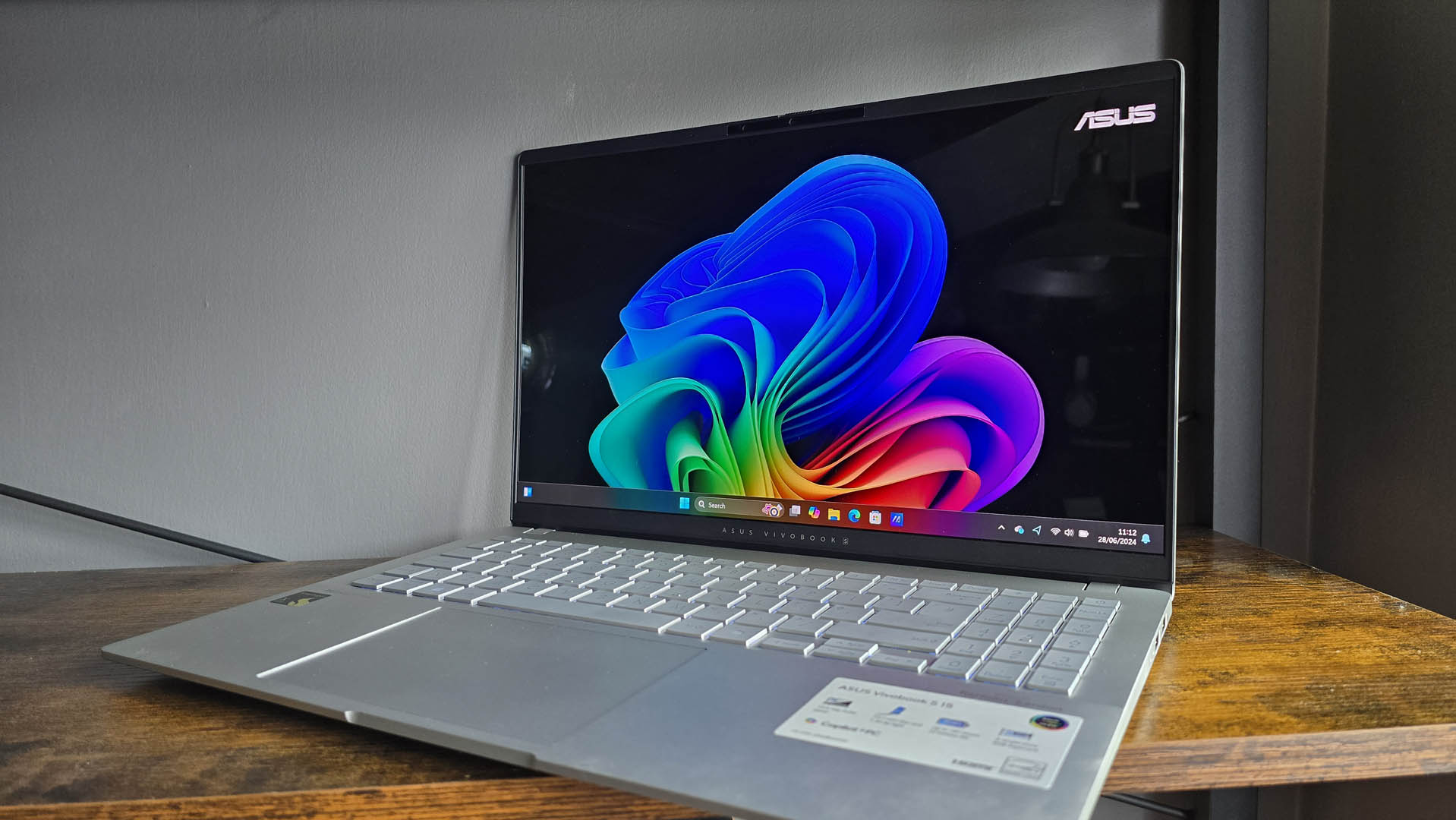 The Asus Vivobook S 15 Copilot+ in silver pictured on a wooden desk.