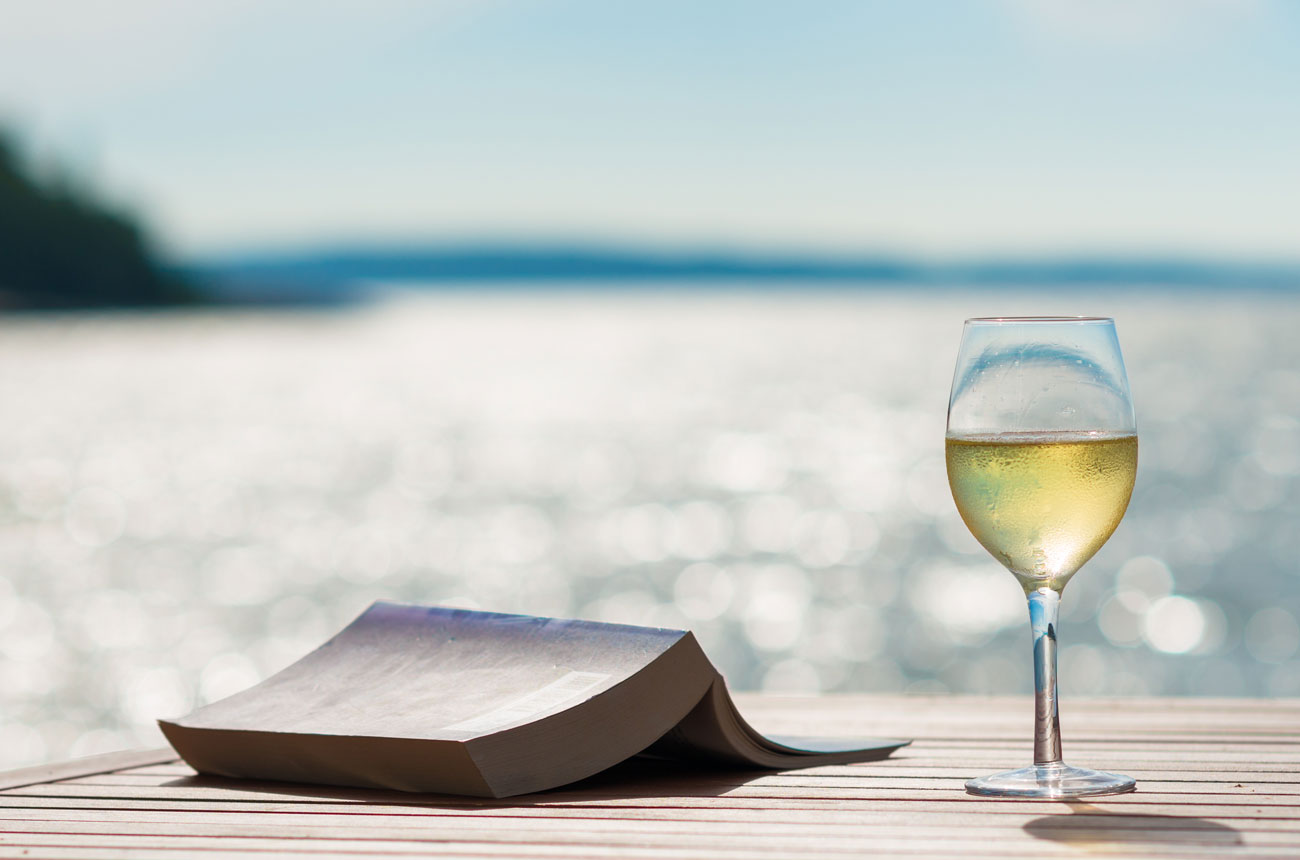 Glass of wine and book against sea background