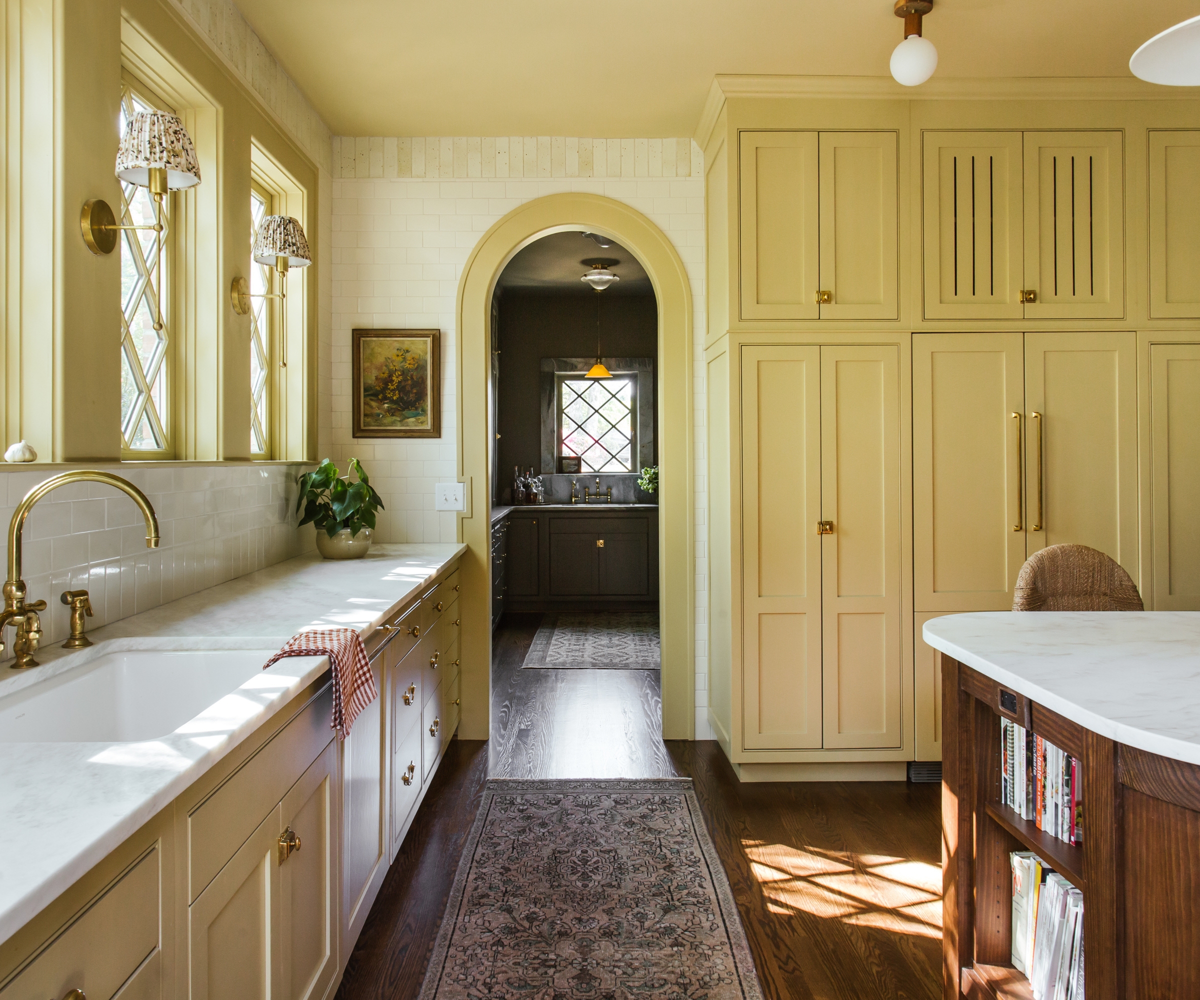 A yellow kitchen with marble countertops, a wooden island, and an arched doorway into the pantry
