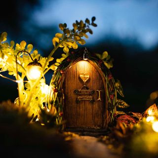 A fairy garden door at night time with a tiny lantern