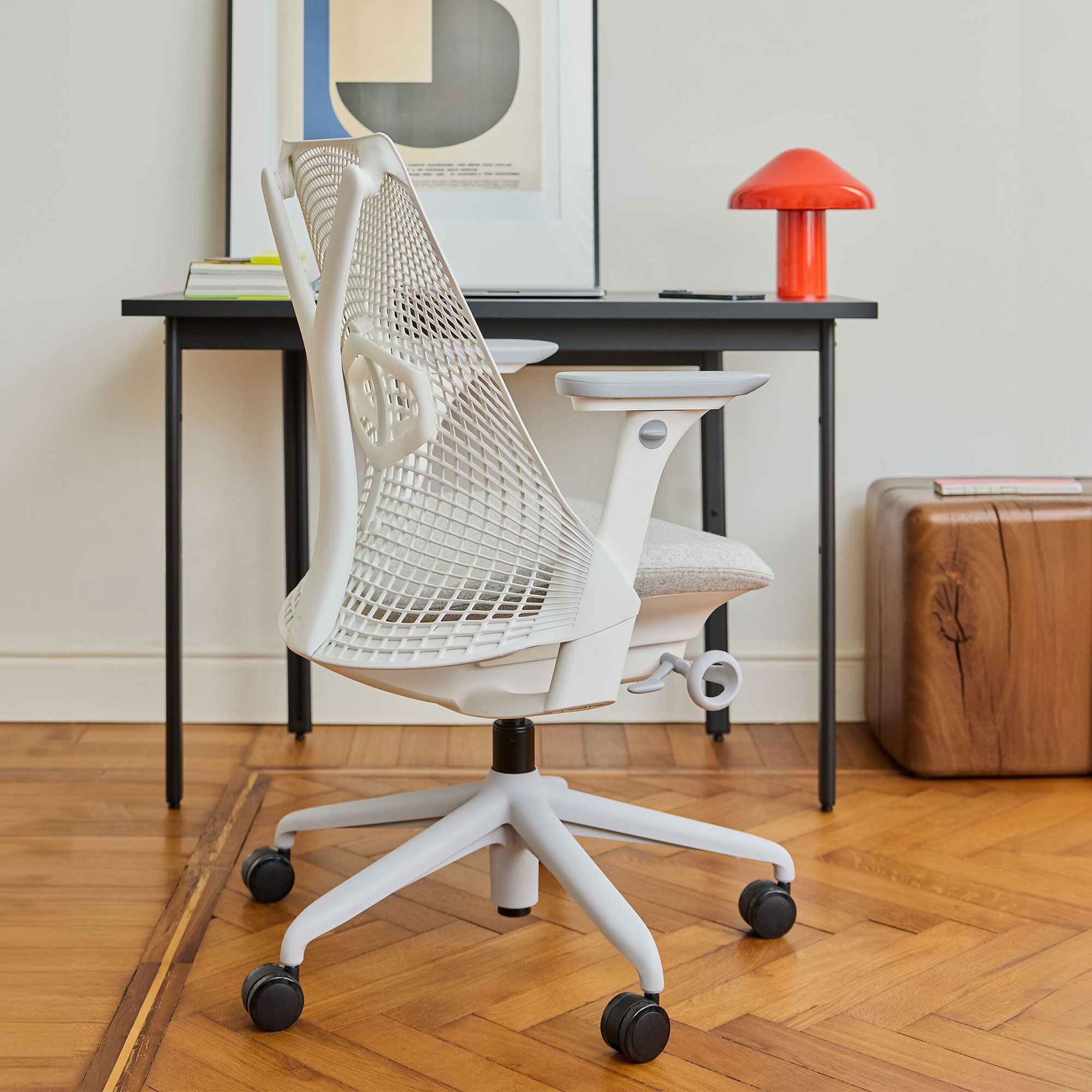 White office chair at dark grey desk with orange wireless lamp and oversized graphic print in thin frame