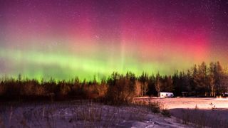 ribbons of green aurora are dominated by a bright scarlet aurora band above against a backdrop of stars.
