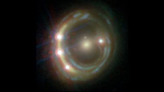 Hubble telescope image of a distant quasar. A ring of light surrounds a yellow spot. There are several bright spots in the ring of light.