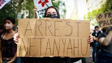 A woman holds up a sign calling for Benjamin Netanyahu&rsquo;s arrest.