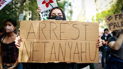 A woman holds up a sign calling for Benjamin Netanyahu&rsquo;s arrest.