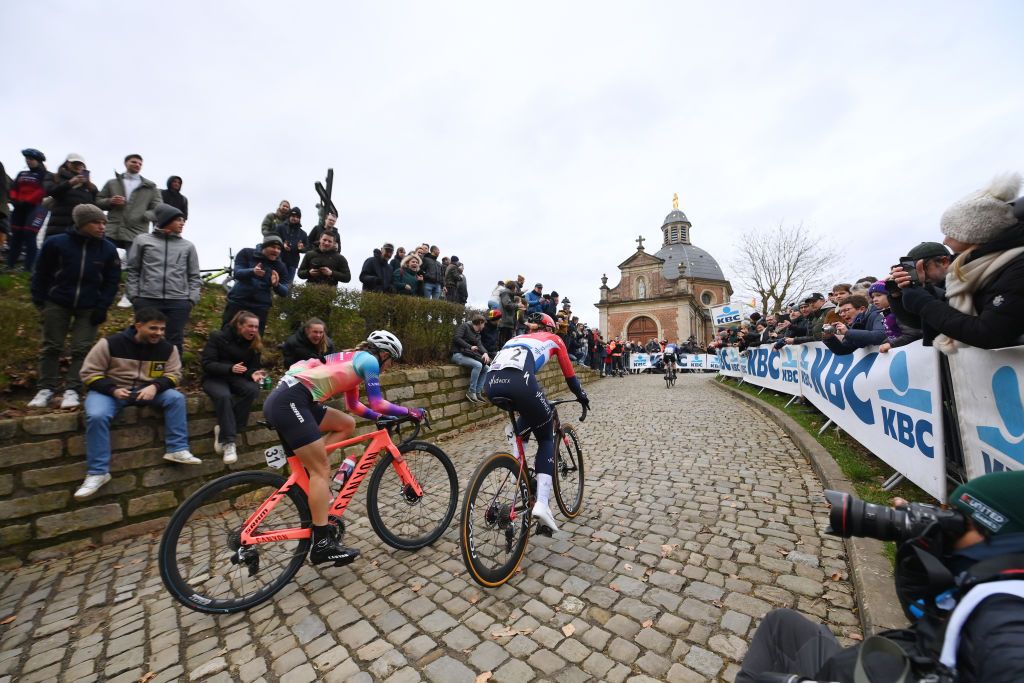 Katarzyna Niewiadoma and Demi Vollering compete climbing the Muur van Geraardsbergen while fans cheer during the 16th Omloop Het Nieuwsblad 2024 