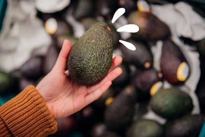 Person holding up a green, ripe avocado in the supermarket, one of the healthy fats