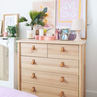 A wooden dresser with leather handles and art prints atop