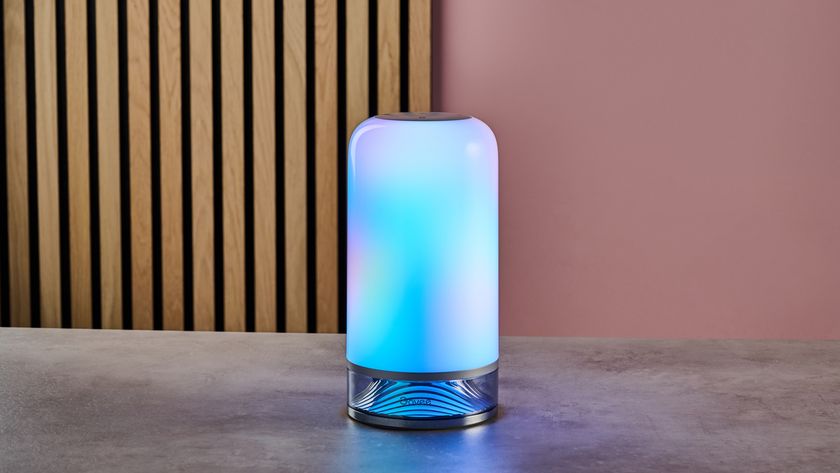 The Govee Table Lamp 2 is lit up with blue and purple colors and sits on a stone surface with wooden slats and a pink wall behind.