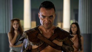 Ashur stands between two women, who are in the background